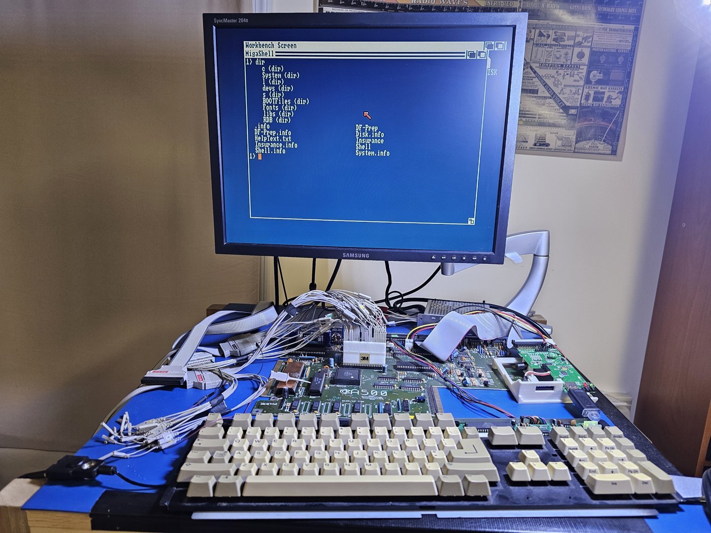 A bare Amiga 500 motherboard on a blue antistatic mat, with logic analyzer leads concentrated around Paula and a monitor showing a Workbench Shell